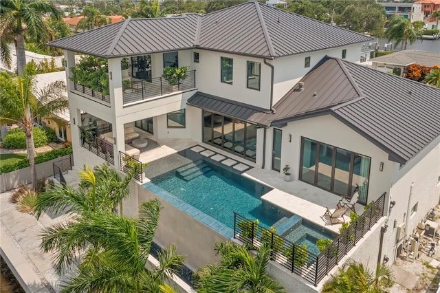 rear view of property with a swimming pool with hot tub, a balcony, and a patio area