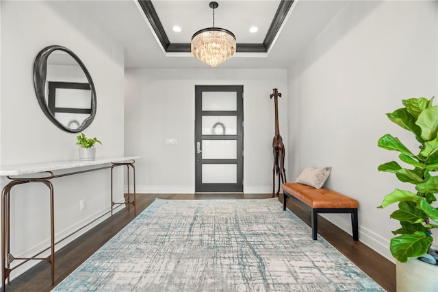 foyer with a raised ceiling, crown molding, dark hardwood / wood-style floors, and a notable chandelier