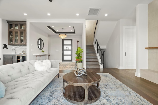 living room with dark hardwood / wood-style floors, indoor wet bar, beverage cooler, and a tray ceiling