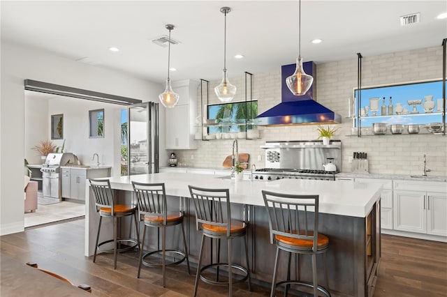 kitchen with white cabinetry, a large island, wall chimney exhaust hood, decorative light fixtures, and decorative backsplash