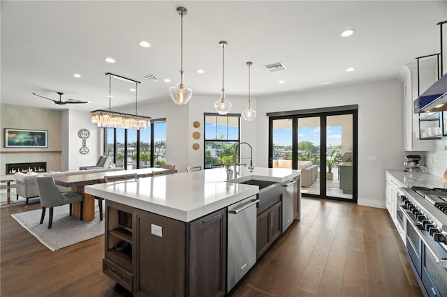 kitchen featuring hanging light fixtures, stainless steel appliances, a kitchen island with sink, a fireplace, and dark brown cabinets