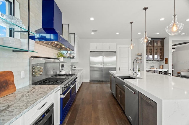 kitchen with wall chimney exhaust hood, backsplash, an island with sink, white cabinets, and high end appliances