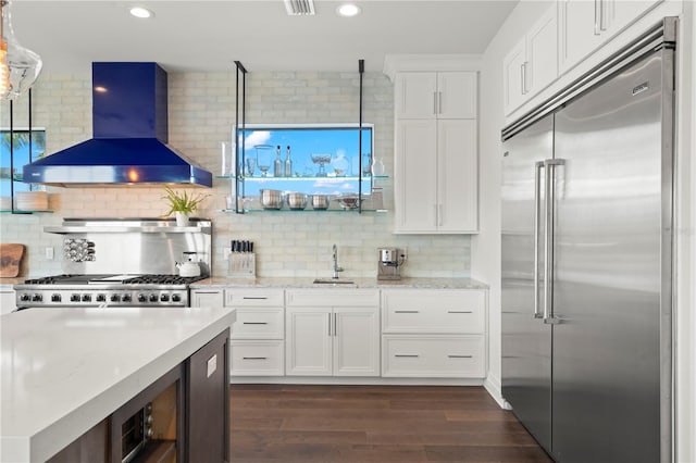 kitchen featuring decorative backsplash, white cabinetry, stainless steel built in fridge, and wall chimney exhaust hood