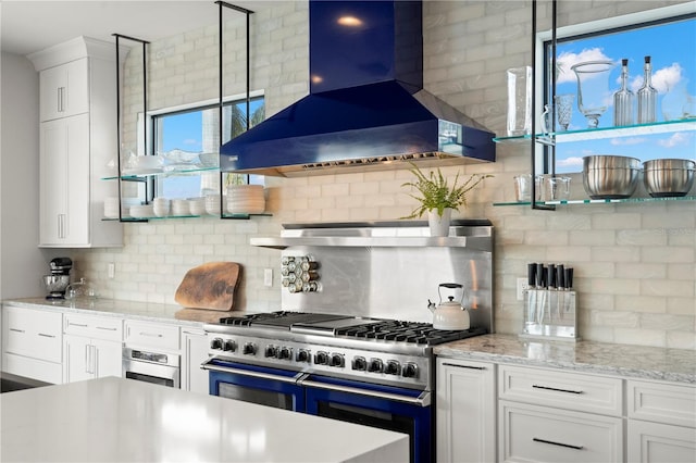 kitchen with appliances with stainless steel finishes, backsplash, light stone counters, wall chimney range hood, and white cabinets