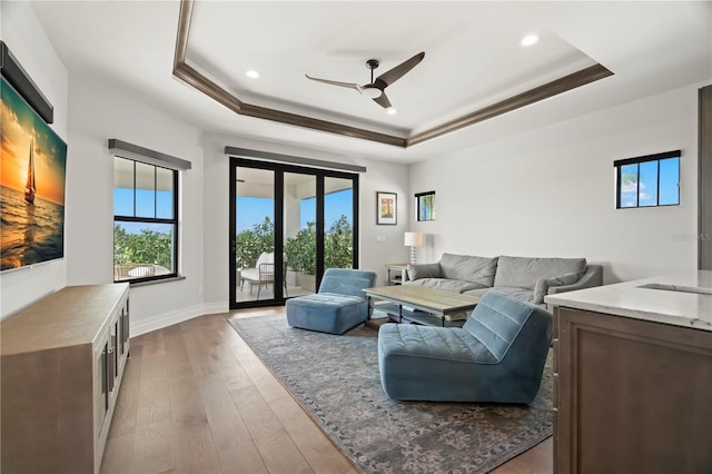 living room featuring a tray ceiling, ceiling fan, crown molding, and light wood-type flooring