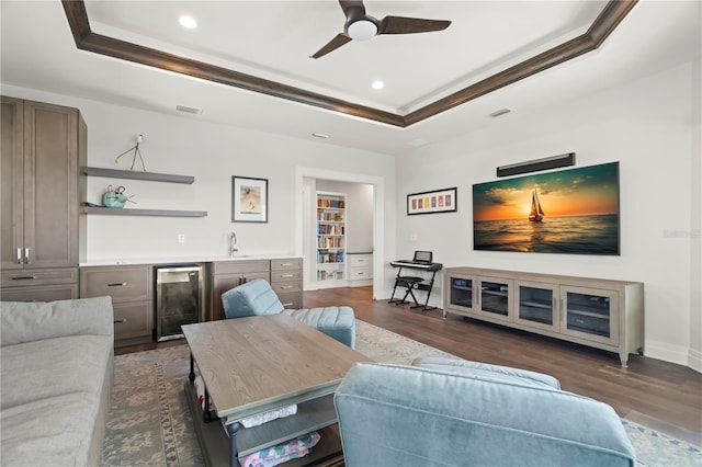 living room with a tray ceiling, wine cooler, crown molding, and dark hardwood / wood-style flooring