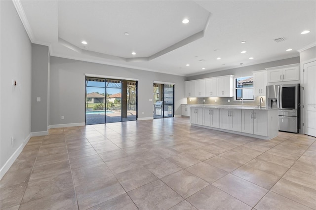 kitchen with a kitchen island, stainless steel refrigerator with ice dispenser, a tray ceiling, crown molding, and white cabinets