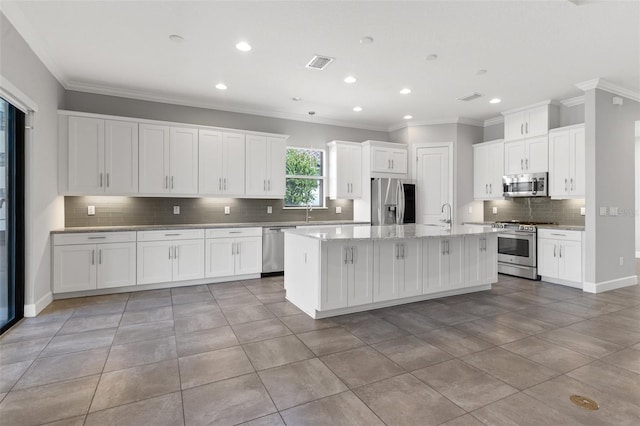 kitchen with stainless steel appliances, a center island with sink, crown molding, light stone countertops, and white cabinetry