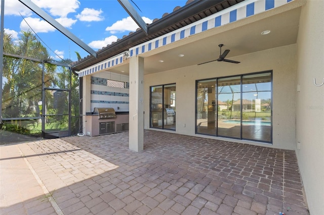 view of patio featuring ceiling fan, an outdoor kitchen, a grill, and glass enclosure