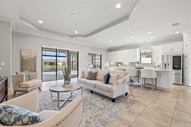 living room with a raised ceiling, light tile patterned floors, recessed lighting, and ornamental molding