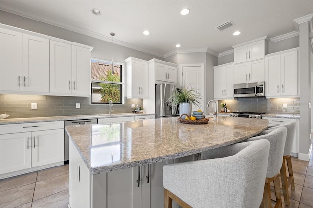 kitchen with appliances with stainless steel finishes, a kitchen bar, a center island with sink, and white cabinets