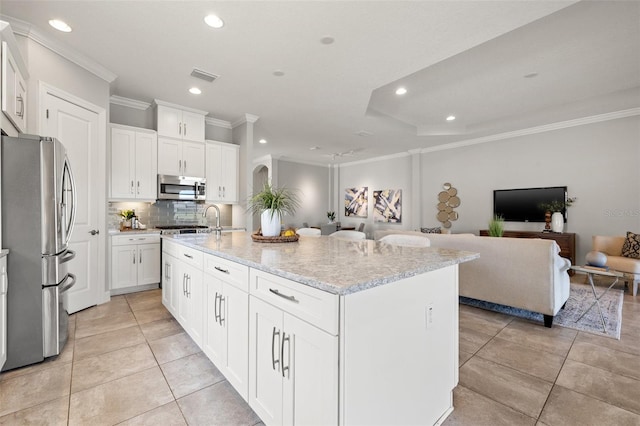 kitchen with white cabinets, an island with sink, light stone counters, appliances with stainless steel finishes, and open floor plan