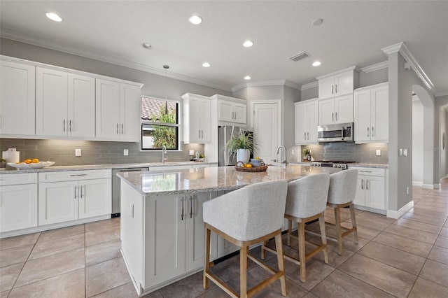 kitchen featuring a center island with sink, visible vents, white cabinets, appliances with stainless steel finishes, and light stone counters