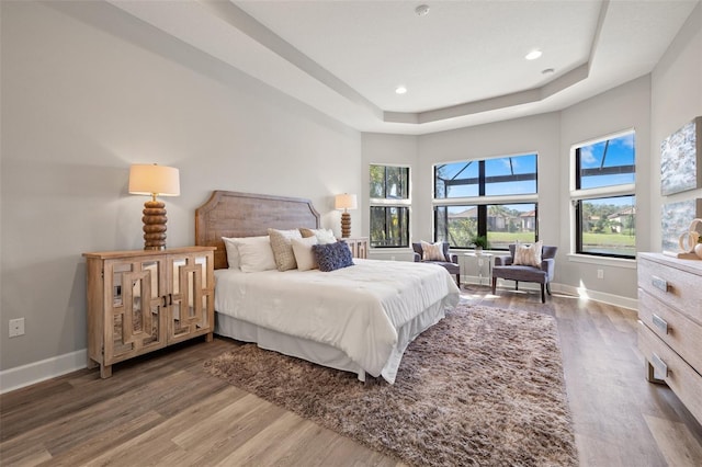 bedroom featuring a tray ceiling, dark wood finished floors, and baseboards