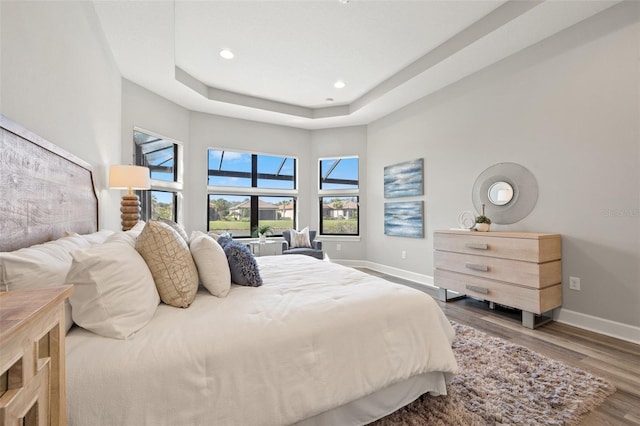 bedroom featuring a raised ceiling, recessed lighting, wood finished floors, and baseboards