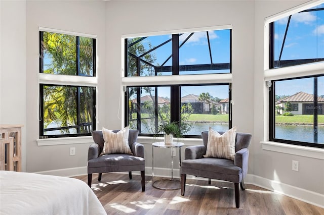 bedroom with baseboards, a water view, a towering ceiling, and light wood finished floors