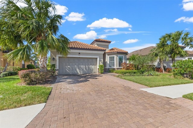 mediterranean / spanish house featuring a tile roof, an attached garage, decorative driveway, a front lawn, and stucco siding