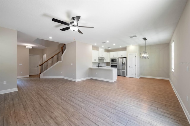 unfurnished living room with sink, light wood-type flooring, and ceiling fan with notable chandelier