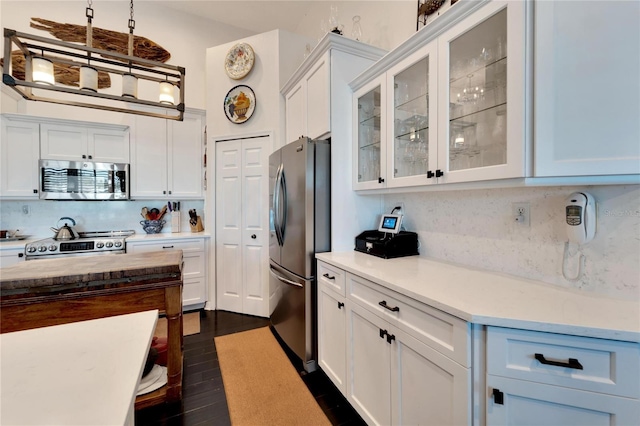 kitchen with appliances with stainless steel finishes, hanging light fixtures, white cabinets, and dark hardwood / wood-style flooring