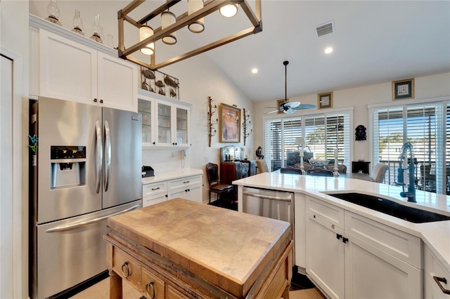 kitchen with appliances with stainless steel finishes, white cabinets, sink, and vaulted ceiling