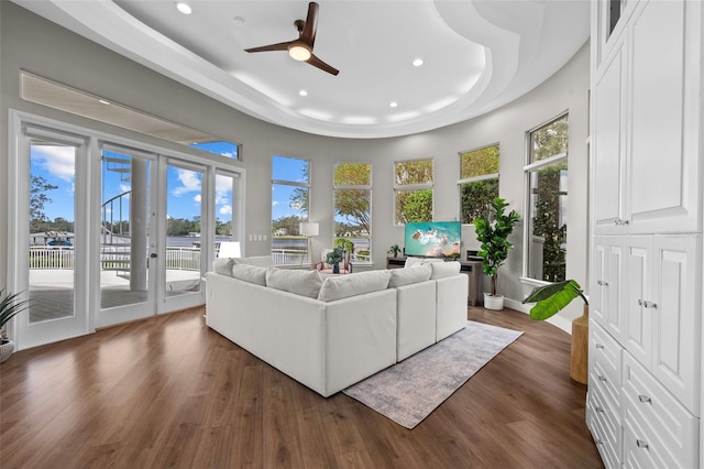 living room with a raised ceiling, dark wood-type flooring, and ceiling fan