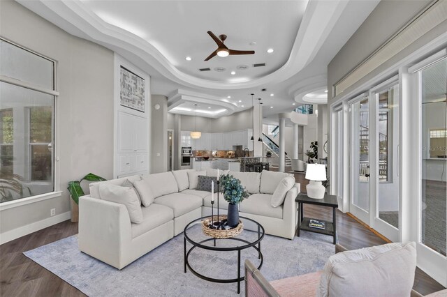 living room featuring wood-type flooring, a wealth of natural light, ceiling fan, and a tray ceiling