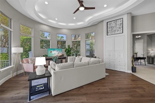 living room with ceiling fan, a tray ceiling, dark wood-type flooring, and a healthy amount of sunlight