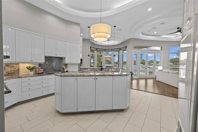 kitchen with dark stone countertops, hanging light fixtures, a tray ceiling, and white cabinets