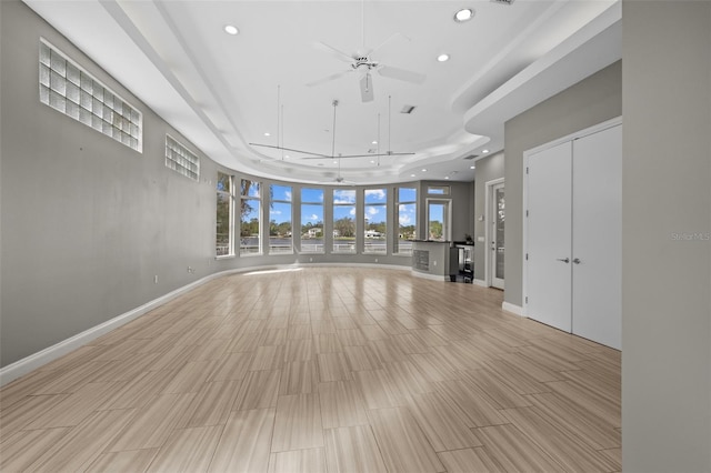 unfurnished living room featuring ceiling fan, a tray ceiling, and light hardwood / wood-style flooring