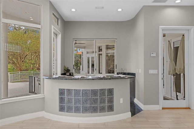 bar with dark stone countertops, a healthy amount of sunlight, and sink