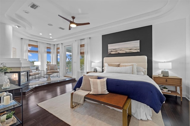 bedroom featuring access to exterior, a tray ceiling, a fireplace, and dark wood-type flooring