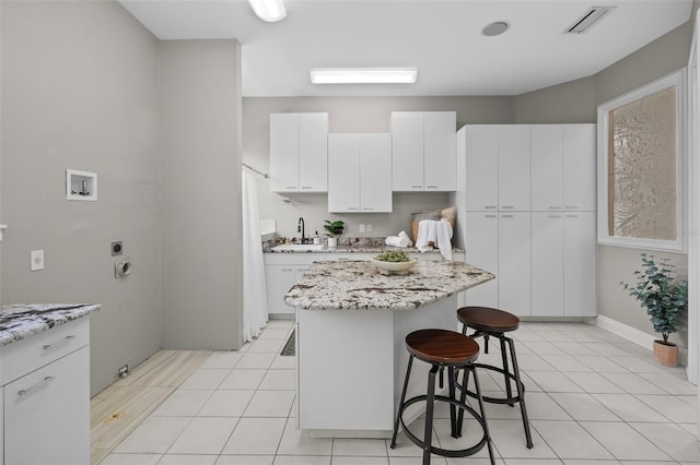 kitchen with light tile patterned flooring, white cabinetry, a kitchen bar, a center island, and light stone counters