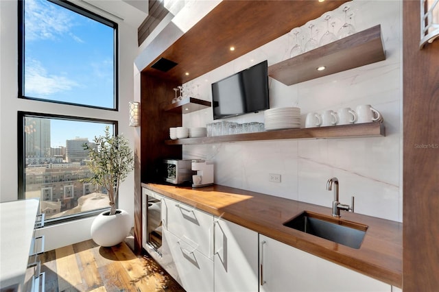 bar featuring sink, light hardwood / wood-style flooring, decorative backsplash, butcher block countertops, and white cabinetry