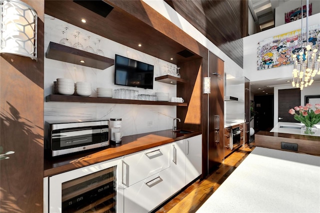 bar with wood counters, white cabinets, sink, decorative light fixtures, and beverage cooler