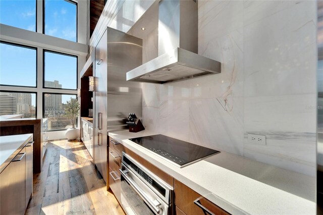 kitchen featuring wall chimney exhaust hood, black electric cooktop, light hardwood / wood-style flooring, a high ceiling, and oven