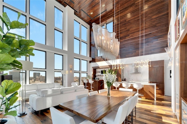 dining room featuring light hardwood / wood-style flooring, plenty of natural light, a towering ceiling, a chandelier, and wood ceiling