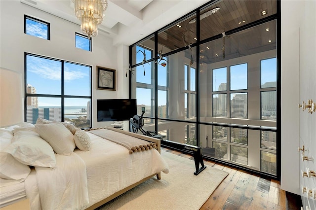 bedroom featuring wood-type flooring, a towering ceiling, and a chandelier