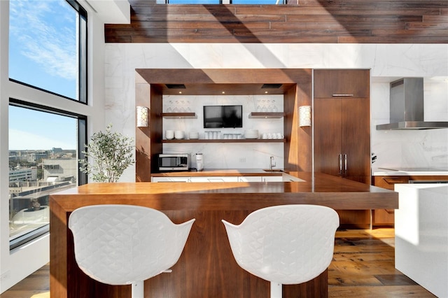 bar with tasteful backsplash, wall chimney exhaust hood, cooktop, sink, and dark hardwood / wood-style floors