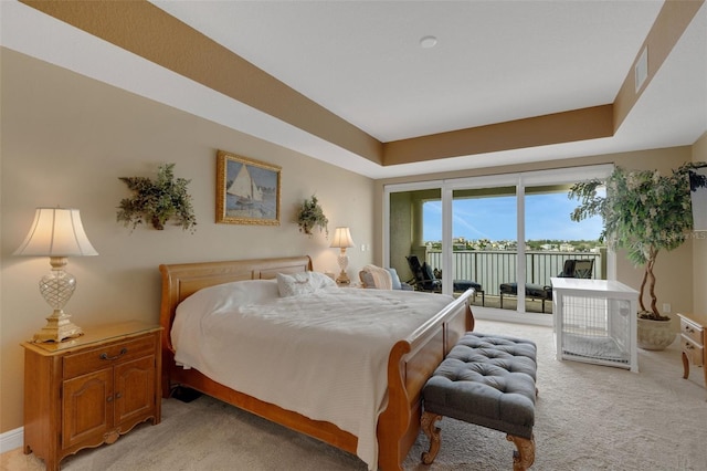 bedroom with light carpet, a raised ceiling, and access to exterior