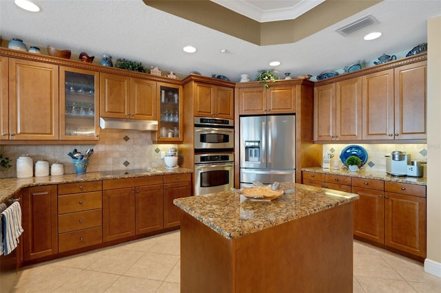 kitchen featuring backsplash, a textured ceiling, a center island, stainless steel appliances, and light stone counters