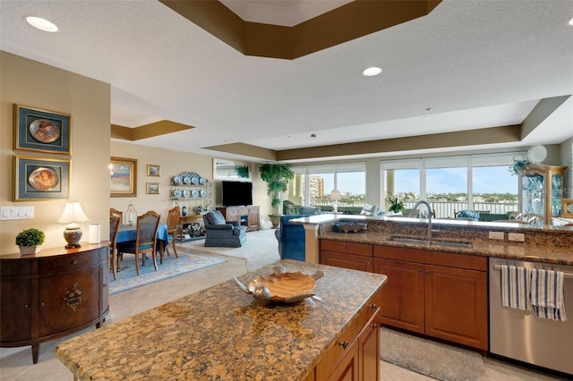 kitchen featuring a raised ceiling, dishwasher, dark stone countertops, sink, and a center island