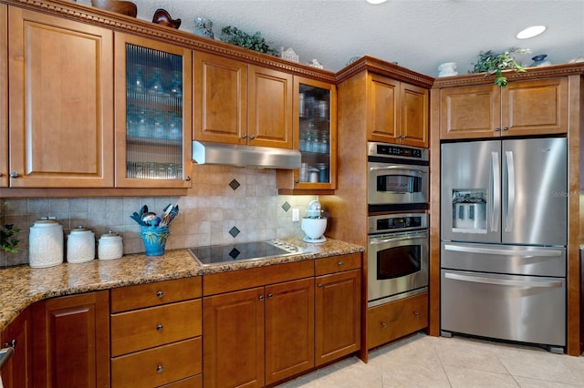 kitchen featuring backsplash, light tile patterned flooring, appliances with stainless steel finishes, light stone counters, and a textured ceiling