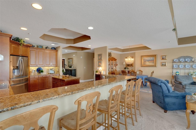 kitchen with stainless steel fridge, light carpet, a tray ceiling, and kitchen peninsula