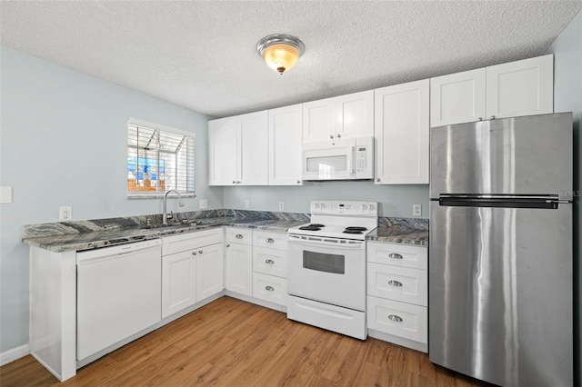 kitchen featuring white appliances, white cabinets, sink, light hardwood / wood-style flooring, and dark stone countertops