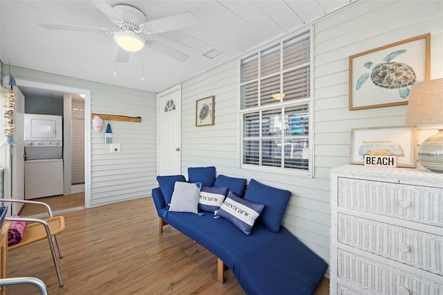 sitting room with wood walls, wood-type flooring, and stacked washer and clothes dryer