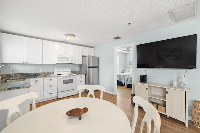 kitchen featuring white cabinetry, sink, dark stone countertops, light hardwood / wood-style floors, and white appliances