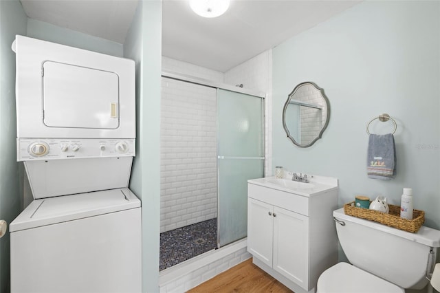 bathroom featuring stacked washing maching and dryer, hardwood / wood-style floors, toilet, a shower with door, and vanity