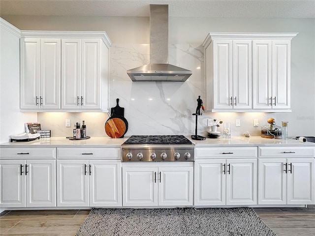 kitchen with decorative backsplash, wall chimney exhaust hood, stainless steel gas stovetop, white cabinets, and light hardwood / wood-style floors