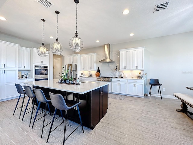 kitchen featuring a large island, wall chimney exhaust hood, pendant lighting, white cabinets, and a breakfast bar area