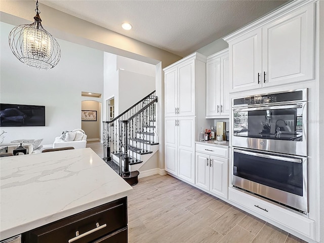 kitchen with light stone countertops, stainless steel double oven, white cabinets, and light hardwood / wood-style flooring